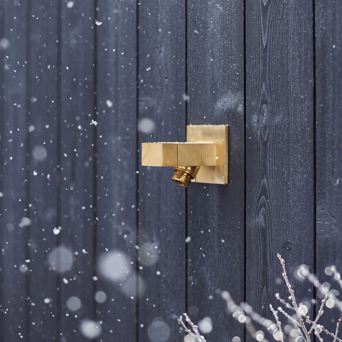 Kula Hydrant in Brushed Brass on dark wood siding in falling snow