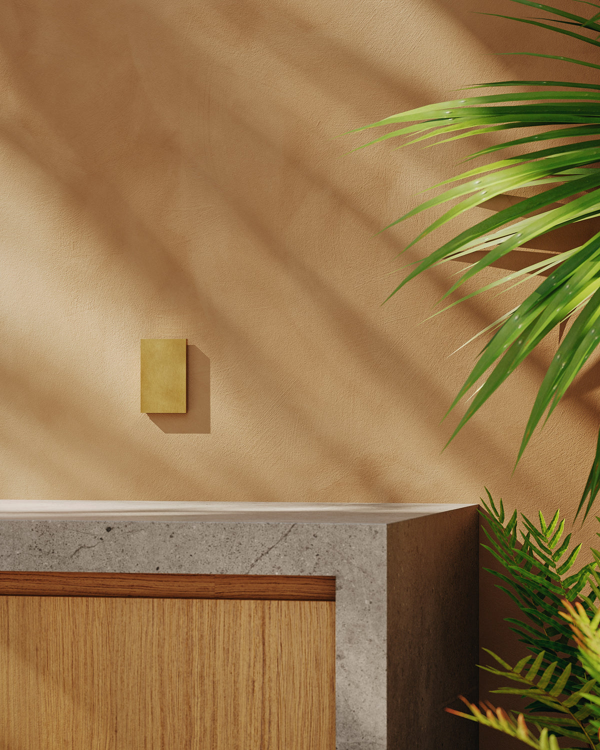 Kula Cover – Vertical in Brushed Aged Brass, closed, on a plaster wall beside palm fronds